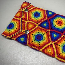Load image into Gallery viewer, A crocheted pouch with a colourful rainbow pattern, featuring two metal buttons on the front, photographed on a neutral grey surface.
