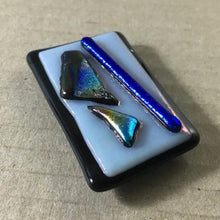 Load image into Gallery viewer, A black and white fused-glass magnet with blue dichroic features.
