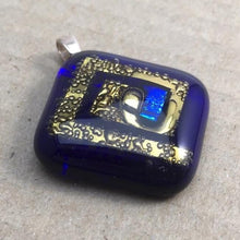 Load image into Gallery viewer, A blue fused-glass pendant with a brass spiral and dichroic spot.
