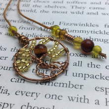 Load image into Gallery viewer, A copper wire tree of life bookmark with yellow and brown beads laying on an open page.
